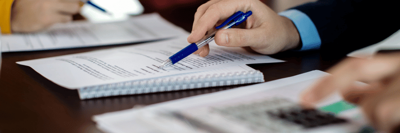 A close-up of hands holding pens and writing on notepads during a meeting, with a calculator nearby.