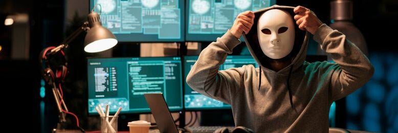 A masked individual adjusting a white mask in a dark room filled with multiple computer screens, symbolizing a hacker targeting a managed services providers network in a cybersecurity attack scenario