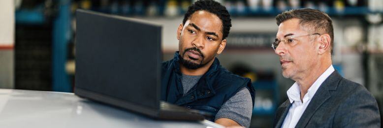 Auto technician and business manager reviewing software on a laptop, discussing recovery measures against CDK hacking