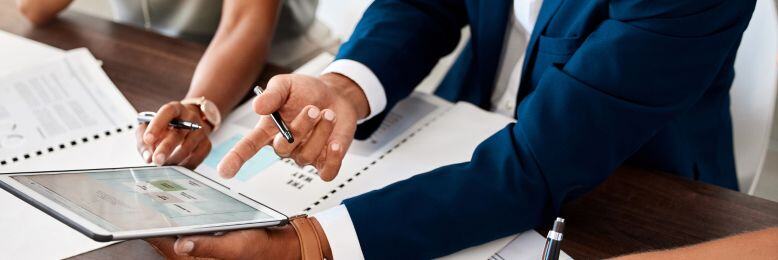 Business professionals analyzing financial data on a tablet during a SOC 2 audit preparation meeting