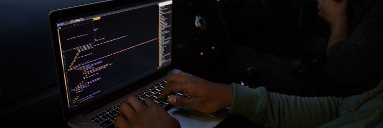 Developer using a laptop in a car, potentially exploring vulnerabilities related to CDK hacking in automotive cybersecurity