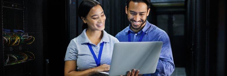 IT professionals consulting in a server room, analyzing public sector outsourcing costs on a laptop