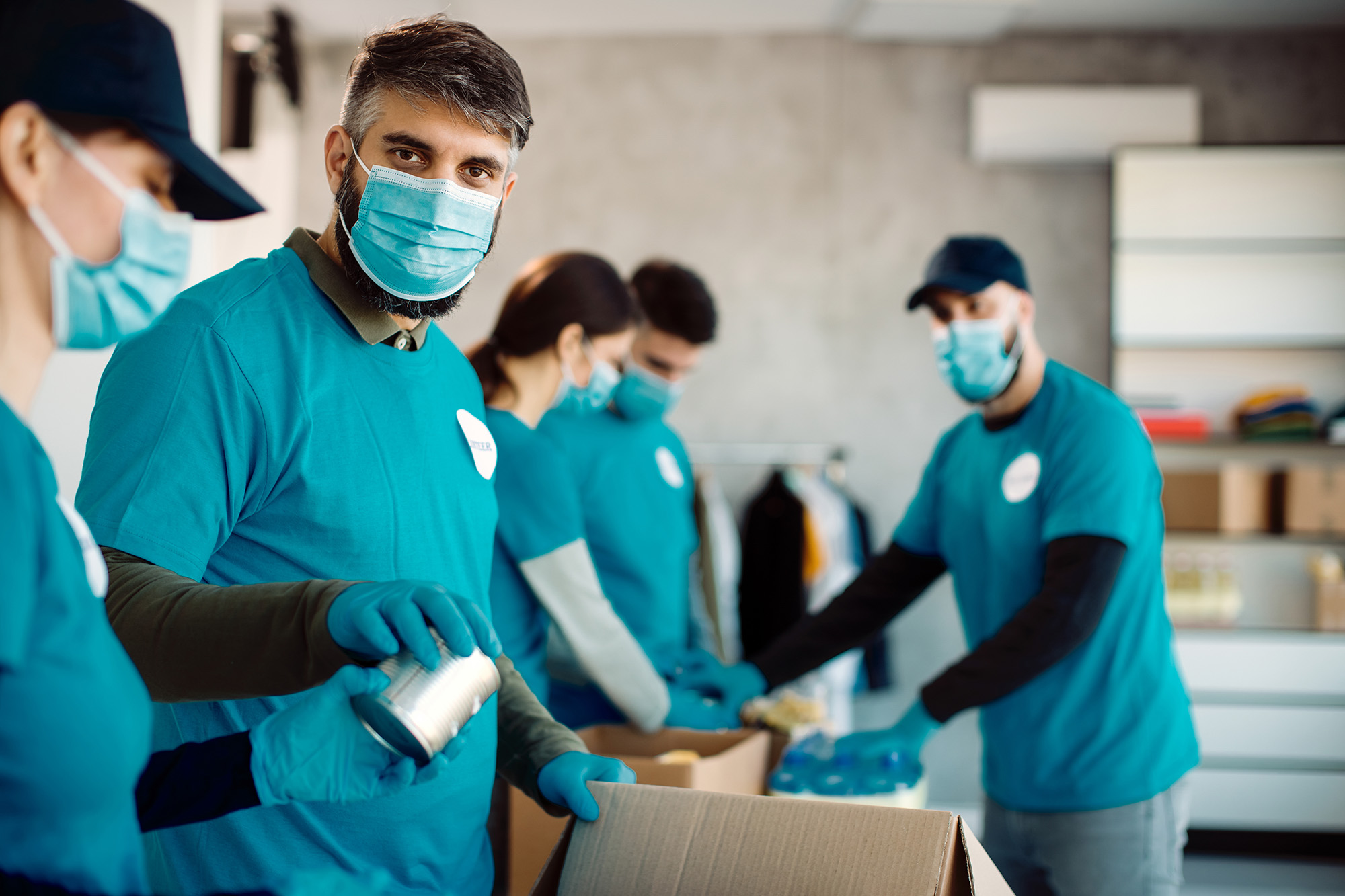 npo_how_step3 (Group of people with protective face masks packing donation boxes for food charity)