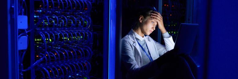 Stressed technician analyzes potential data loss causes in a server room with illuminated racks