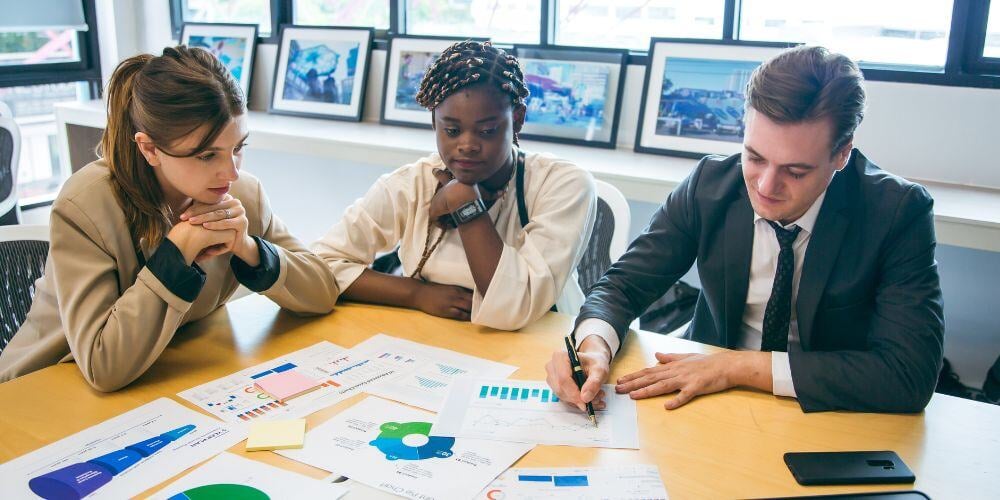 Three colleagues analyzing charts and graphs in a meeting room, focusing on MSP ROI analysis and performance strategies