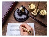 a person holding a pen above a contract with a gavel and scale on the background